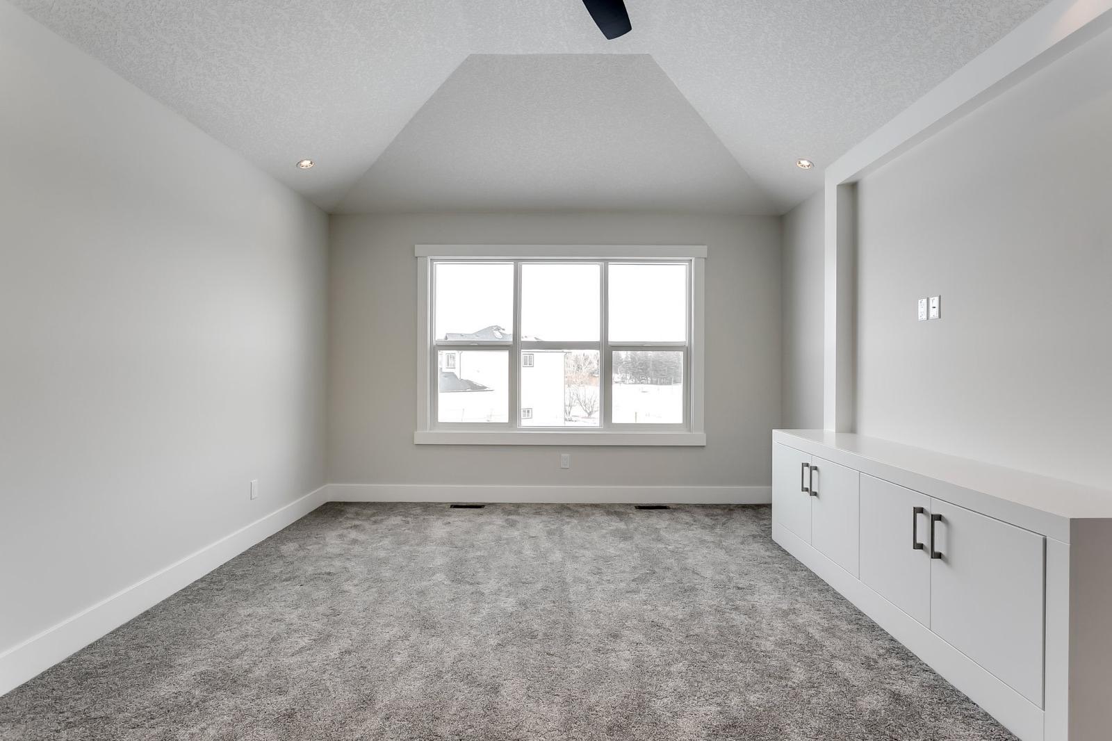 Finished bedroom with painted drywall walls, vaulted ceiling, and built-in cabinetry in a Calgary home