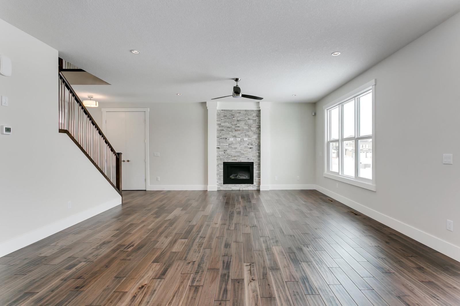 Finished living room with smooth drywall walls, stone fireplace, and staircase in a Calgary home